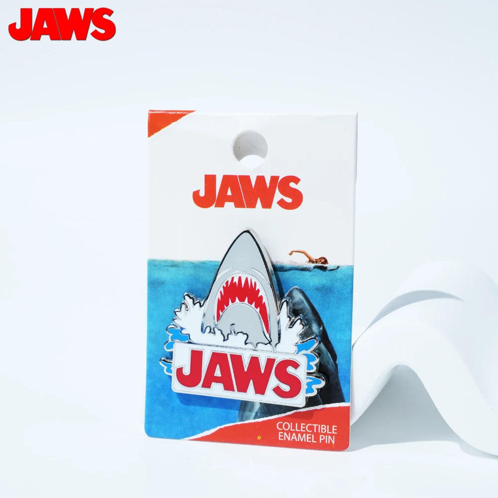 A rectangular packaging for a Jaws collectible enamel pin featuring a shark design.