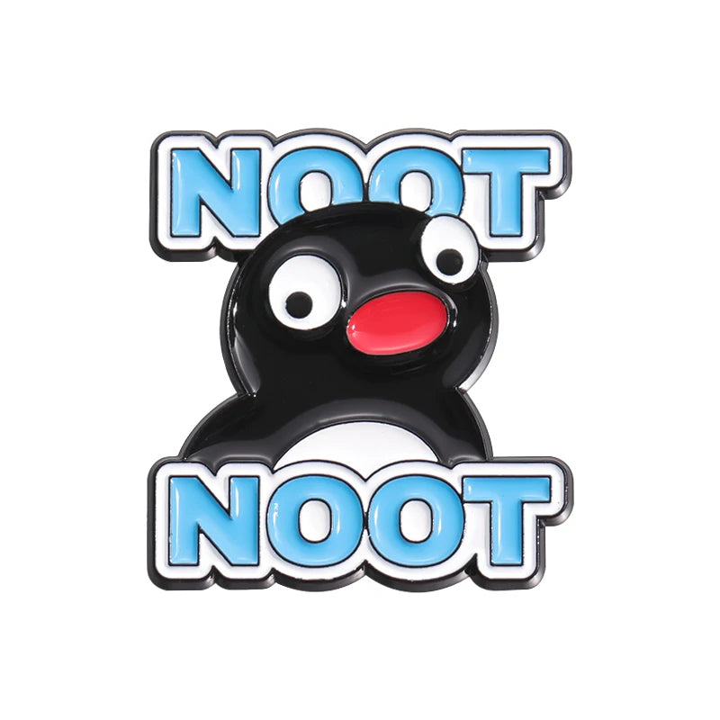 A black cartoon penguin enamel pin with surprised eyes and the word NOOT above and below in light blue.
