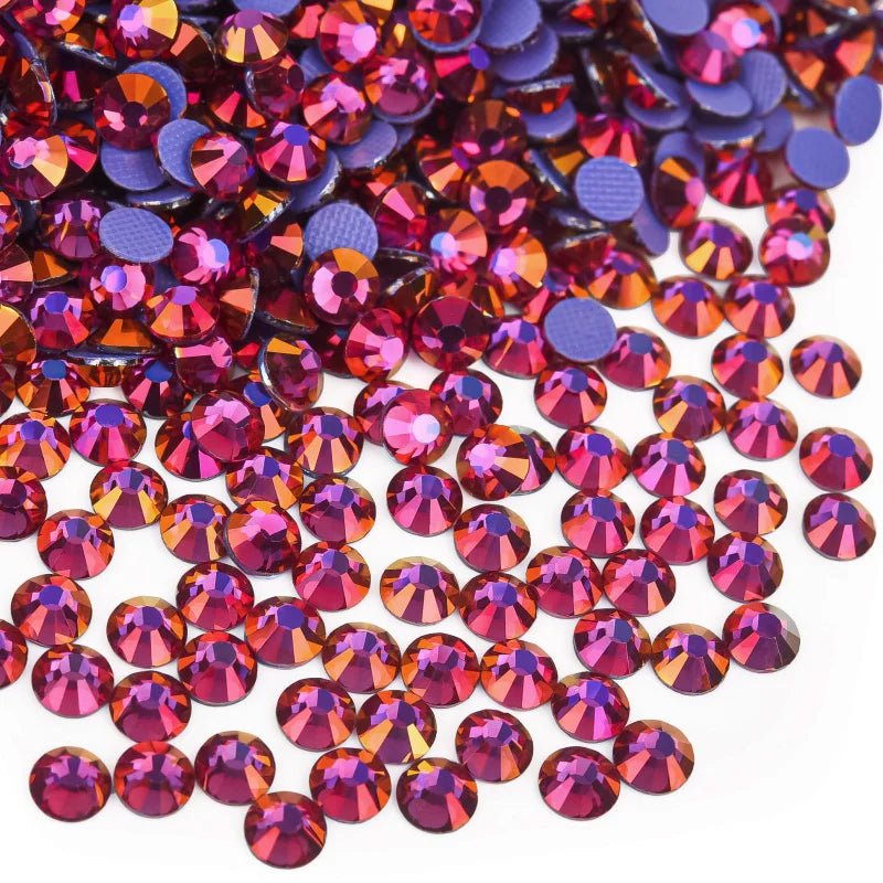 A close-up view of various hotfix rhinestones in shades of pink, purple, and orange scattered on a white background.