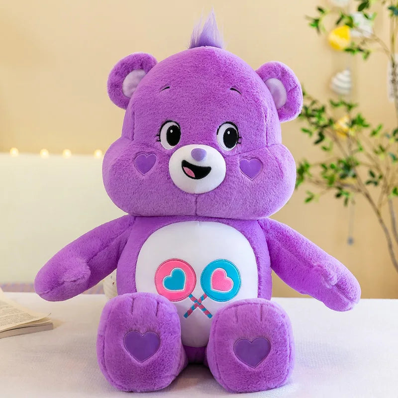 Peluche Kawaii Care Bears arcoíris morado con detalles rosa sobre una superficie blanca.