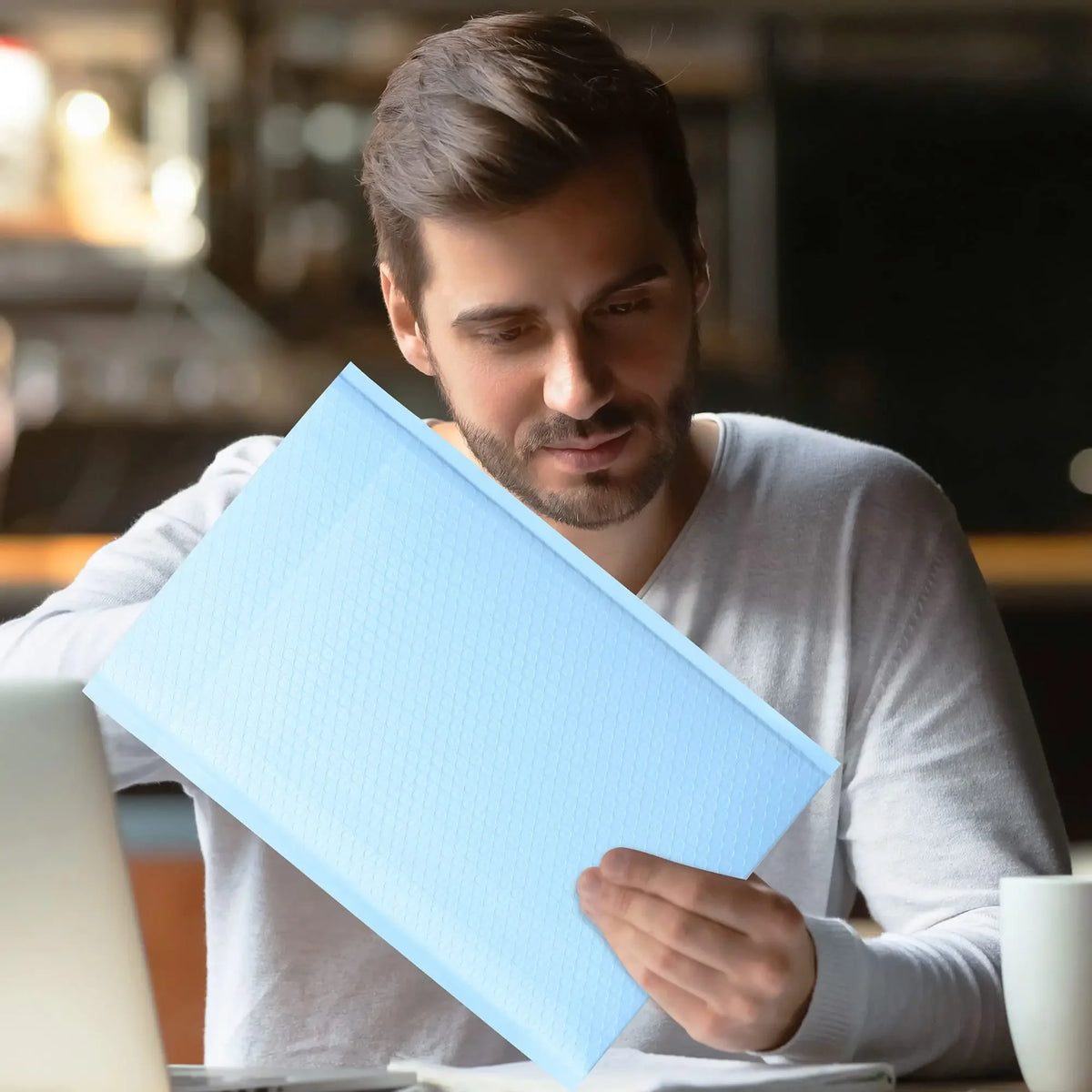 A man is holding a blue bubble mailer shipping envelope in his hands.
