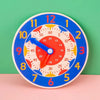 A blue wooden clock face with colorful numbers and hands, set against a green background.