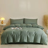 A light sage green quilted duvet cover set displayed on a bed with neutral bedding and a lamp nearby.