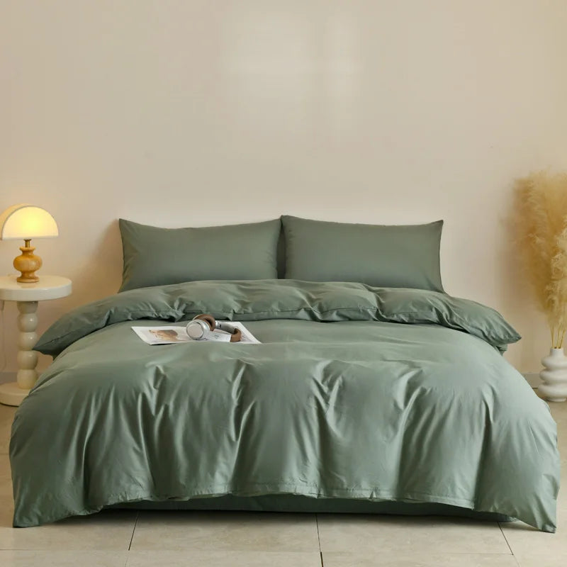 A light sage green quilted duvet cover set displayed on a bed with neutral bedding and a lamp nearby.