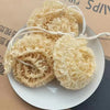 A pile of natural loofah body scrubbers with hanging ropes displayed on a white plate.