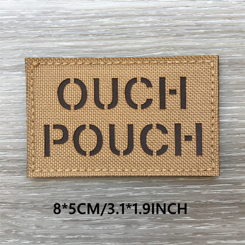 A rectangular tan woven patch with the text OUCH POUCH printed in dark lettering on a wooden surface.