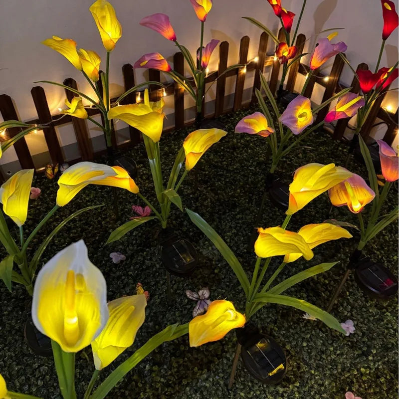 Yellow and pink calla lilies illuminated by solar-powered LED garden lights in a dark setting.