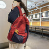 A woman is holding a red and blue patchwork canvas backpack in a casual indoor setting.