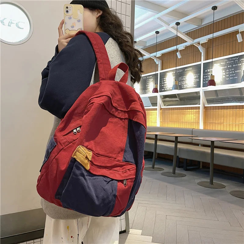 A woman is holding a red and blue patchwork canvas backpack in a casual indoor setting.