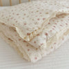 A stack of white floral muslin baby blankets with delicate lace trim resting on a white surface.