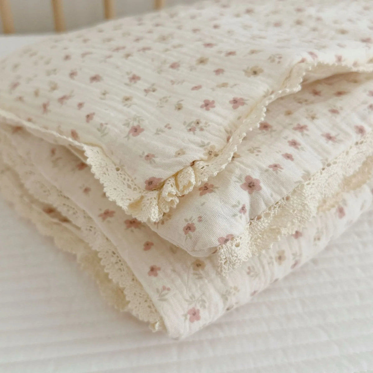 A stack of white floral muslin baby blankets with delicate lace trim resting on a white surface.