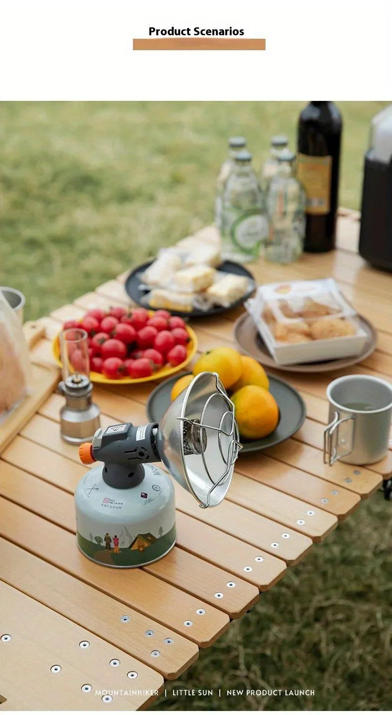 A portable butane gas stove is set up outdoors on a wooden table with various camping and outdoor items.