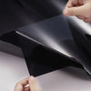 A hand is applying a black car window privacy film to a dark tinted glass surface.