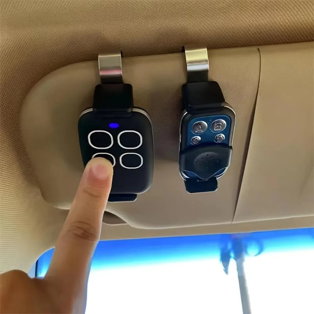 A hand is inserting a black garage door remote into a silver clip holder mounted on a vehicle's interior panel.