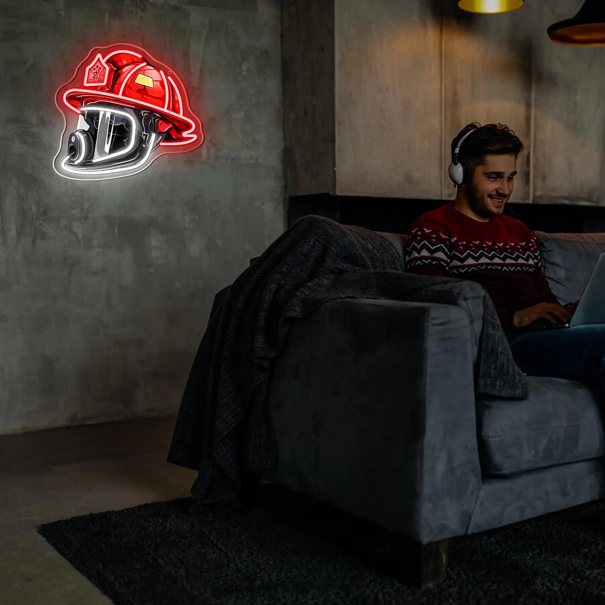 A man sits on a couch in a dimly lit room with a neon firefighter helmet sign glowing on the wall.
