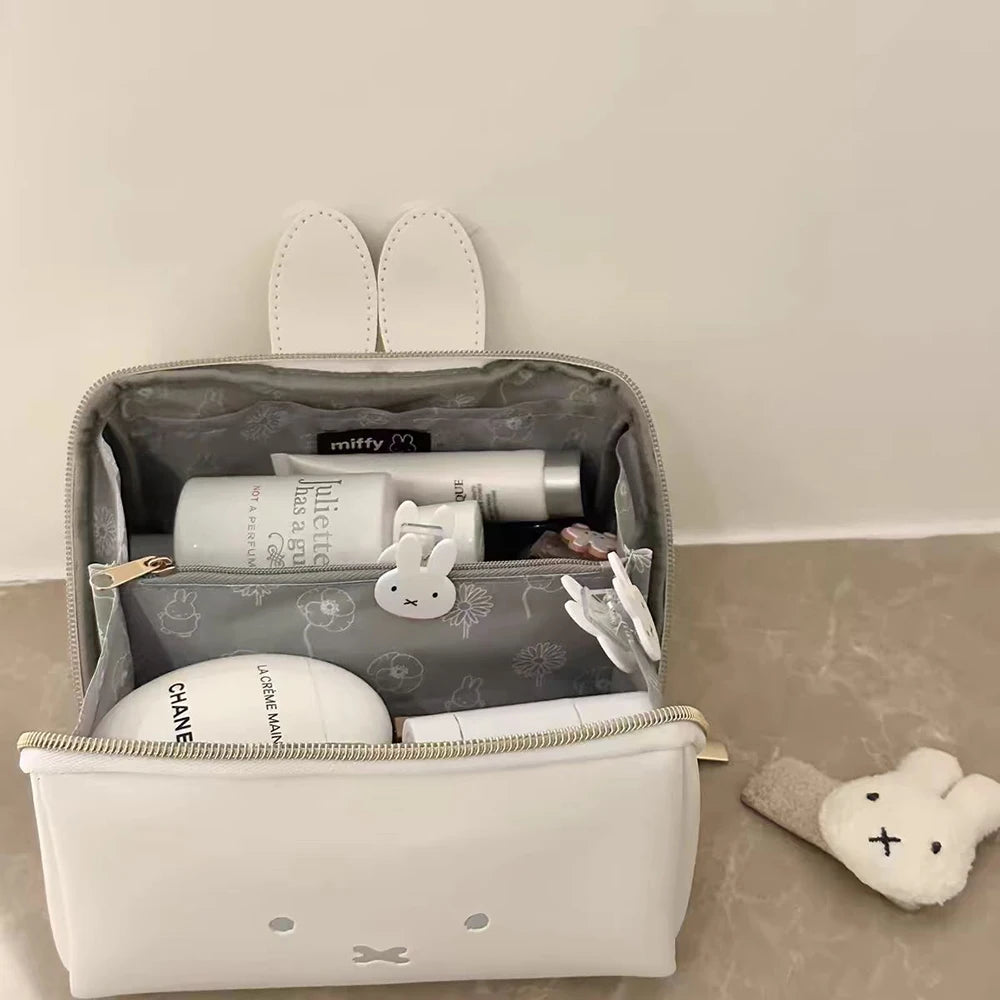 A white cosmetic storage bag with a gray lining and a clear top, featuring Miffy cartoon rabbit accessories.