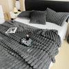 A gray plush cozy fleece blanket draped over a white bed with pillows and a black headboard.