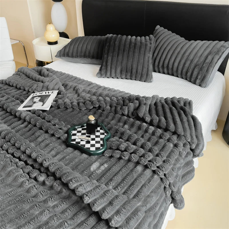 A gray plush cozy fleece blanket draped over a white bed with pillows and a black headboard.