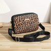 A black leopard print crossbody bag with a gold buckle strap resting on a wooden surface.
