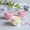 Pink and white silicone rose flower molds with lit candles arranged on a white surface.