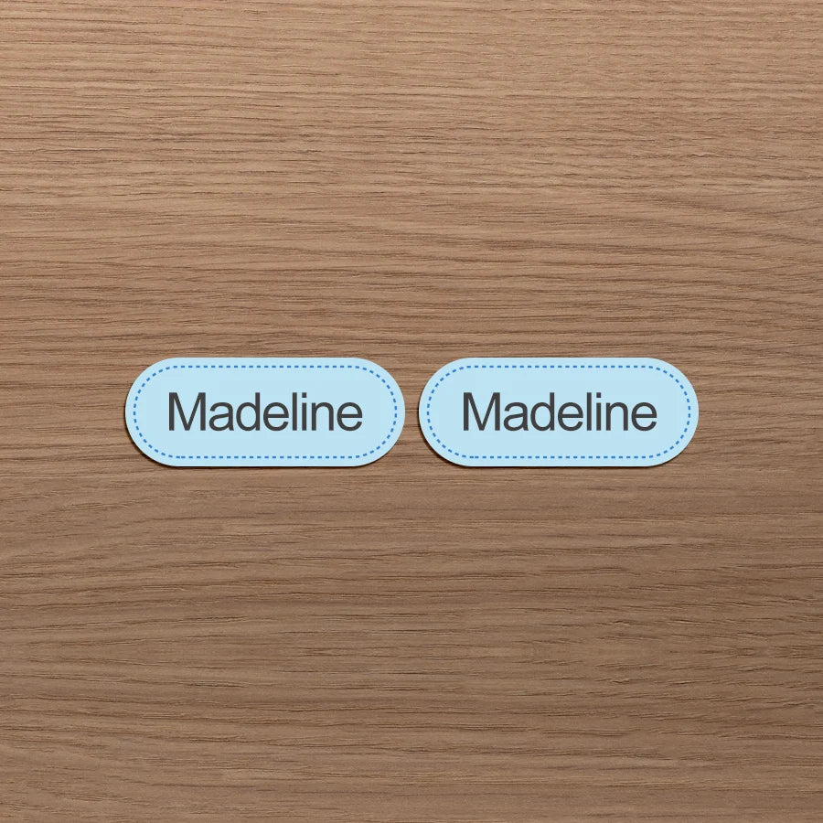 Dos etiquetas ovaladas con el nombre Madeline colocadas sobre una superficie de madera.