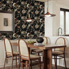 A dining room featuring a wooden table and chairs set against a dark floral wallpaper backdrop.