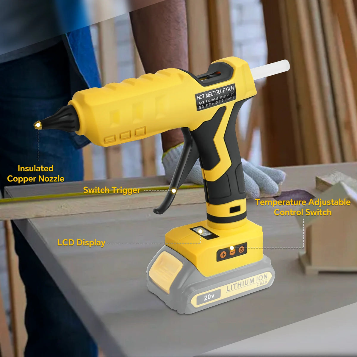 Yellow cordless hot glue gun with insulated copper nozzle and LCD display on a wooden surface.