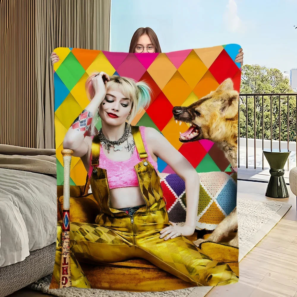 Une femme aux cheveux blonds portant un haut rose et un vêtement jaune à carreaux posant avec une couverture à carreaux color