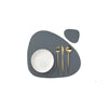 A set of gold-colored cutlery resting on a dark gray placemat with a white plate.