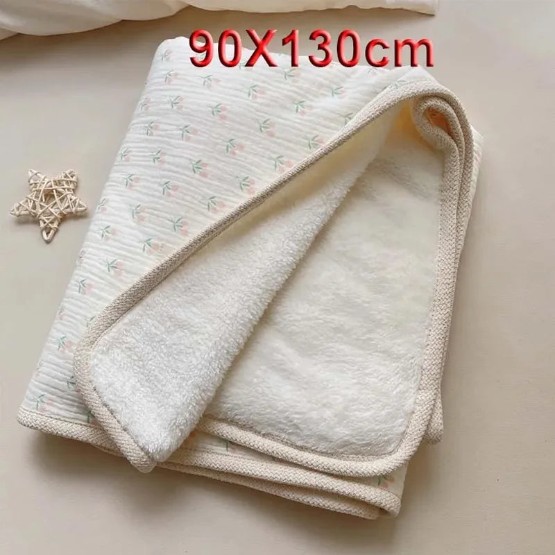 A white floral muslin baby blanket folded and displayed on a light surface.