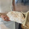 A hand holds a white sequin beaded chain shoulder clutch bag against a light-colored dress.