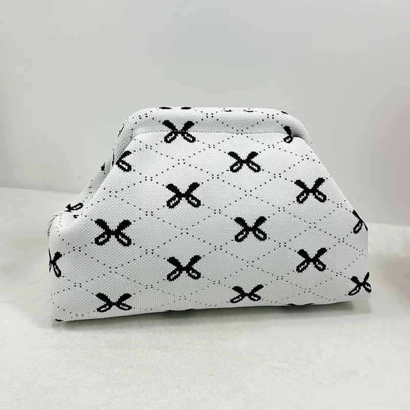 Clutch de tejido blanco con estampado de lazo negro sobre una superficie clara.