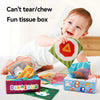 A baby is playing with a fun tissue box filled with colorful cloth books and rings.