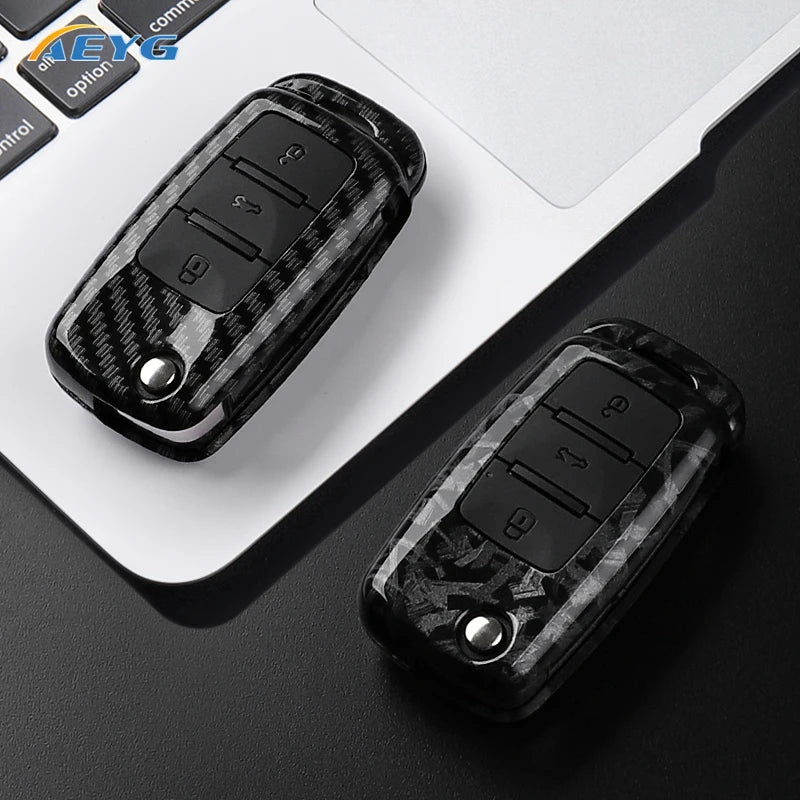 A black carbon fiber car key cover with electronic buttons is shown on a white laptop surface.
