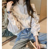 A woman models a cream vintage lace long sleeve blouse and blue jeans.