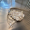 A light beige sequin accent chain shoulder bag with a textured, round design resting on a metallic surface.