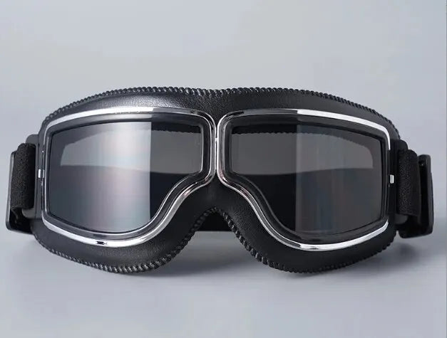 A pair of black retro foldable motorcycle goggles with silver trim are shown against a light gray background.