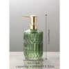 A clear green glass soap dispenser with a gold pump top, shown against a light gray background.