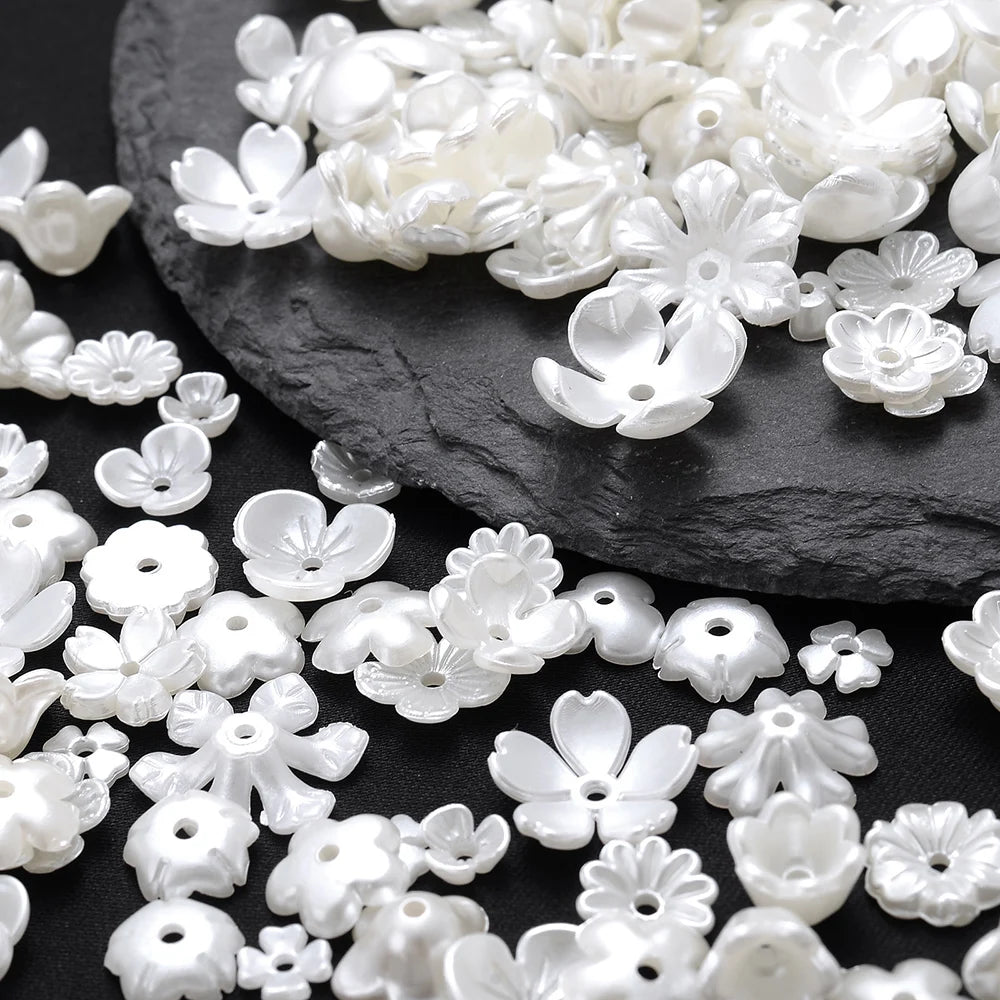A pile of white acrylic pearl spacer beads in various flower shapes scattered on a dark surface.