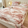 A cozy faux fur fitted sheet in pink and white stripes is displayed on a bed with pillows and a bedside lamp.