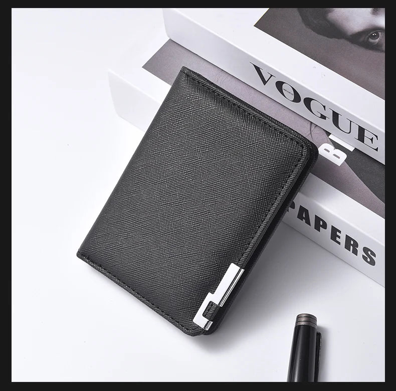 A black slim vertical leather wallet with a silver clasp resting on a white surface next to a magazine.
