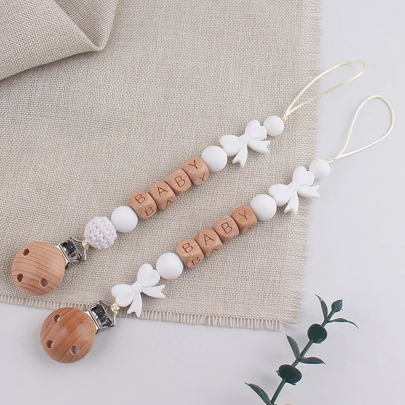 A personalized silicone pacifier clip with a name and anti-drop lanyard featuring white and natural wood elements.