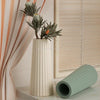 A tall white vase with green foliage sits next to a light green silicone mold.