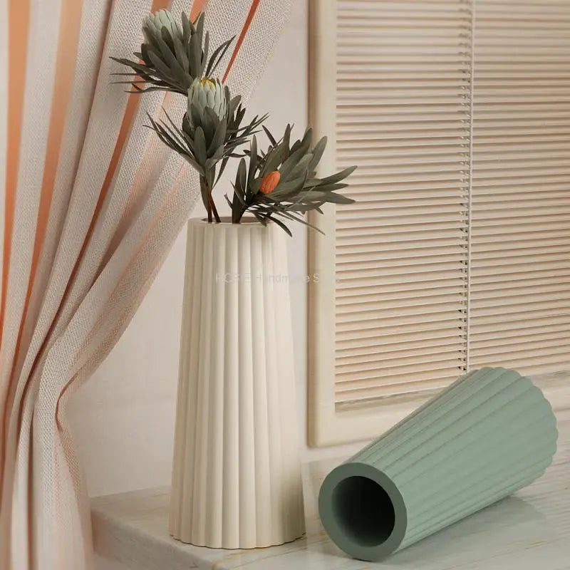 A tall white vase with green foliage sits next to a light green silicone mold.