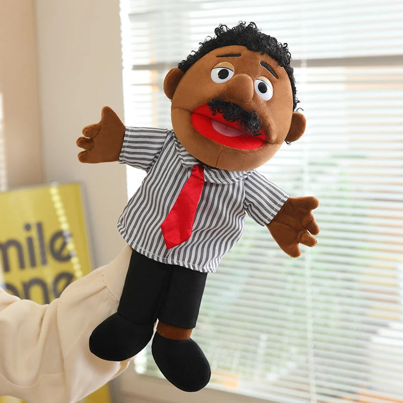 A soft plush full-body hand puppet resembling a man with dark skin, a mustache, and a red tie, standing in front of a window.