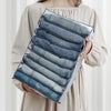 A hand holds a clear foldable closet organizer box filled with neatly folded denim underwear and socks.