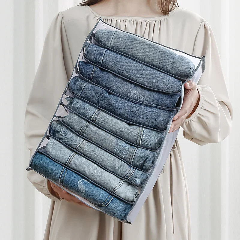 A hand holds a clear foldable closet organizer box filled with neatly folded denim underwear and socks.