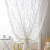 White ruffled French lace sheer curtains with floral embroidery draped in a window.