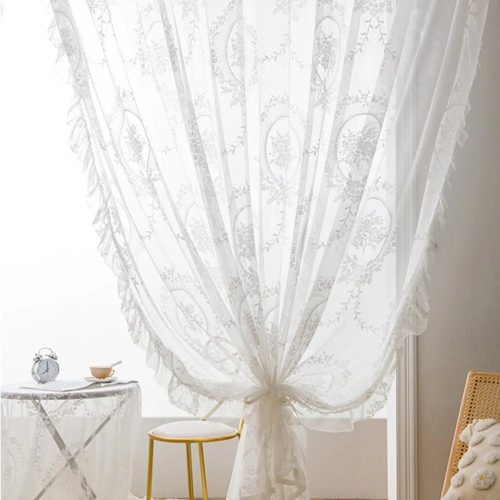 White ruffled French lace sheer curtains with floral embroidery draped in a window.