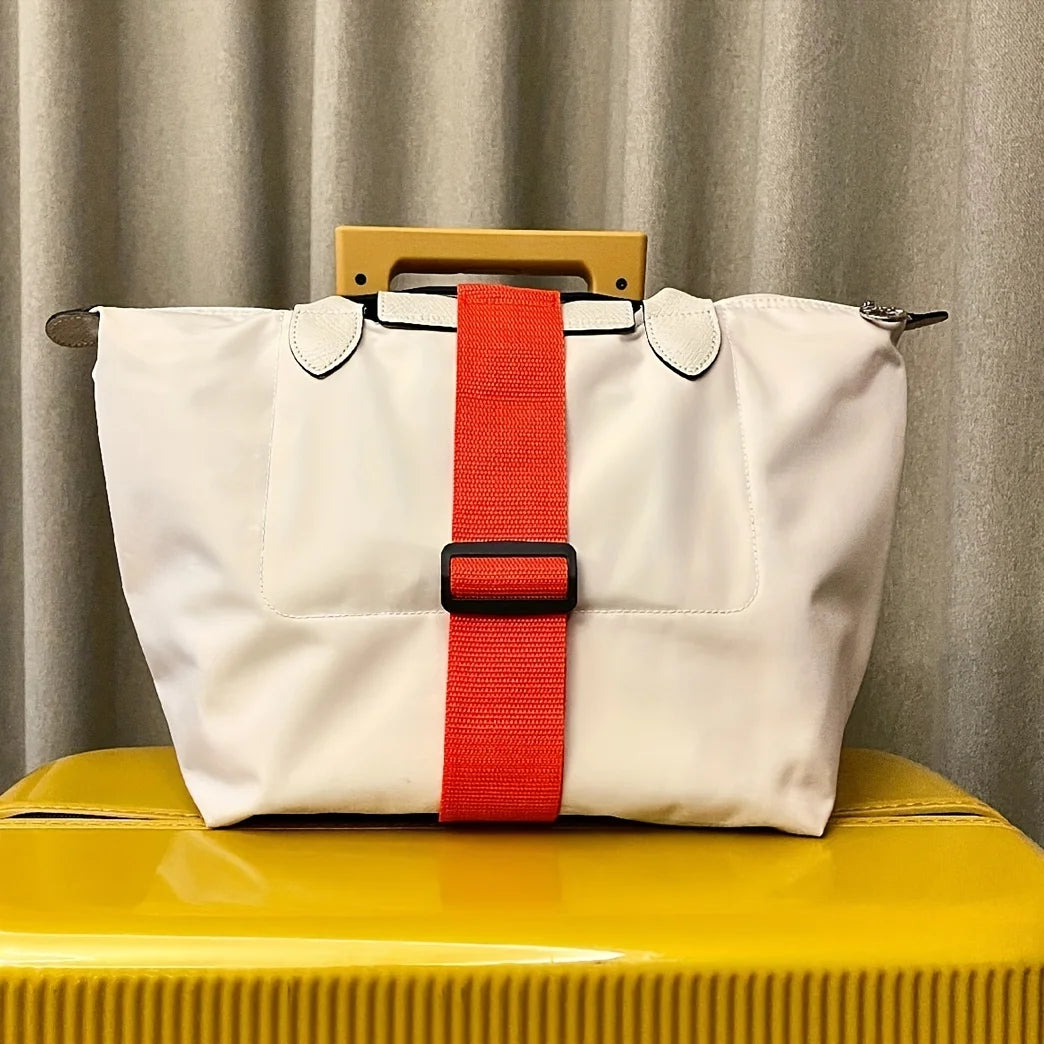A white reusable elastic luggage strap with an orange-red strap and a wooden handle resting on a yellow surface.